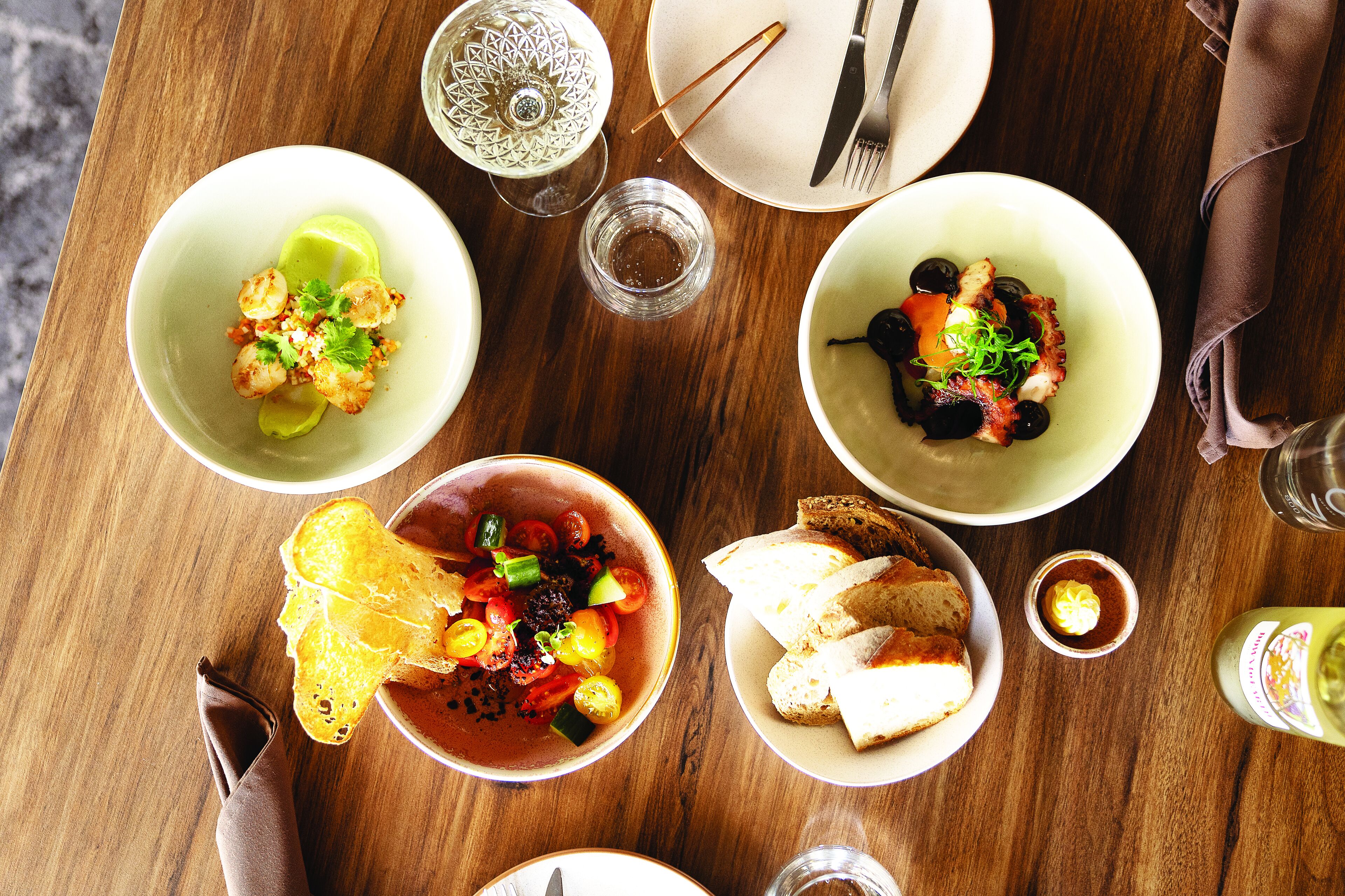 Una mesa de comedor con diversos platos, incluyendo mariscos, verduras y pan.