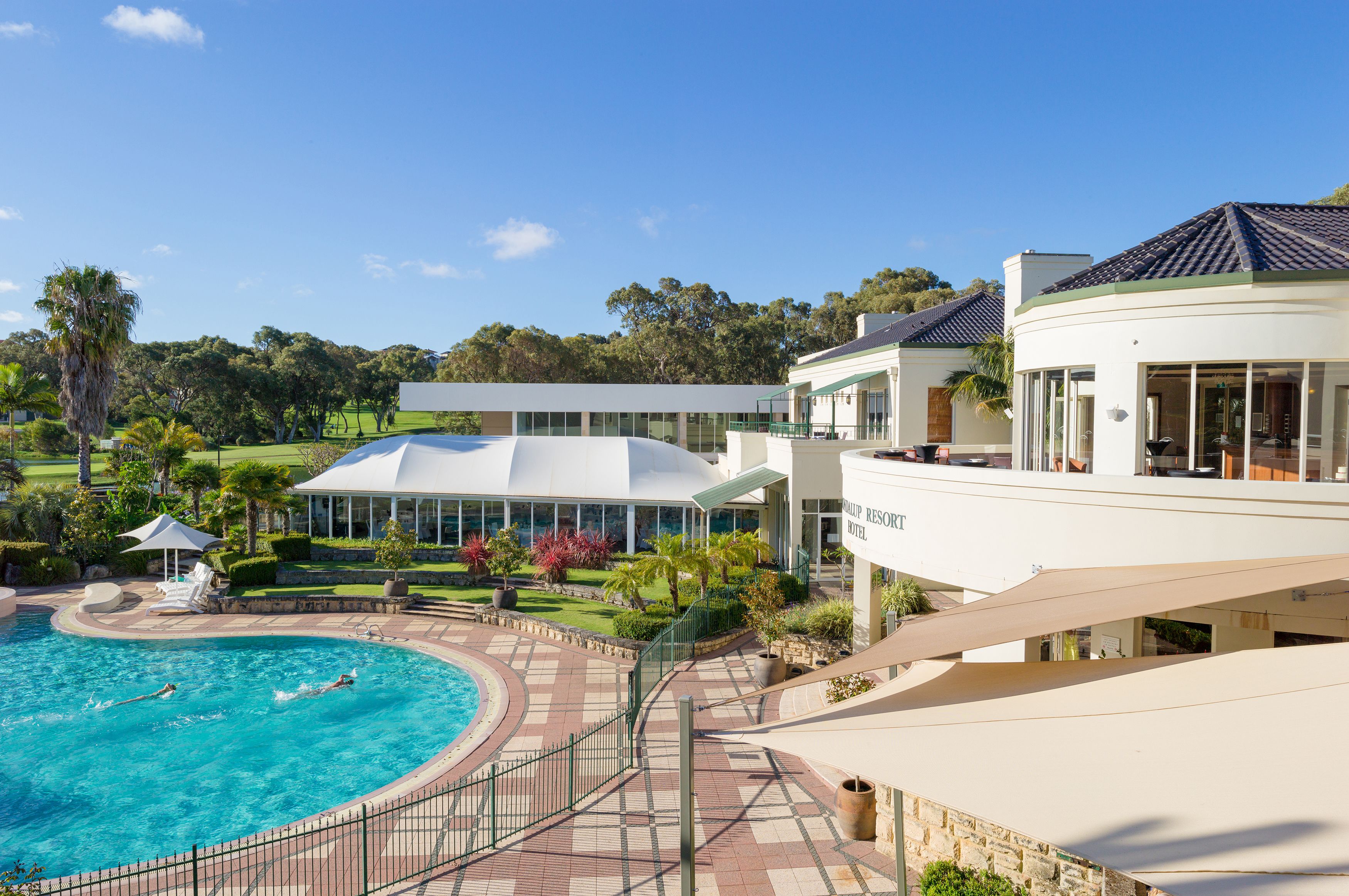 Un resort con piscina, campo de golf y un edificio de fachada blanca y amplios ventanales.