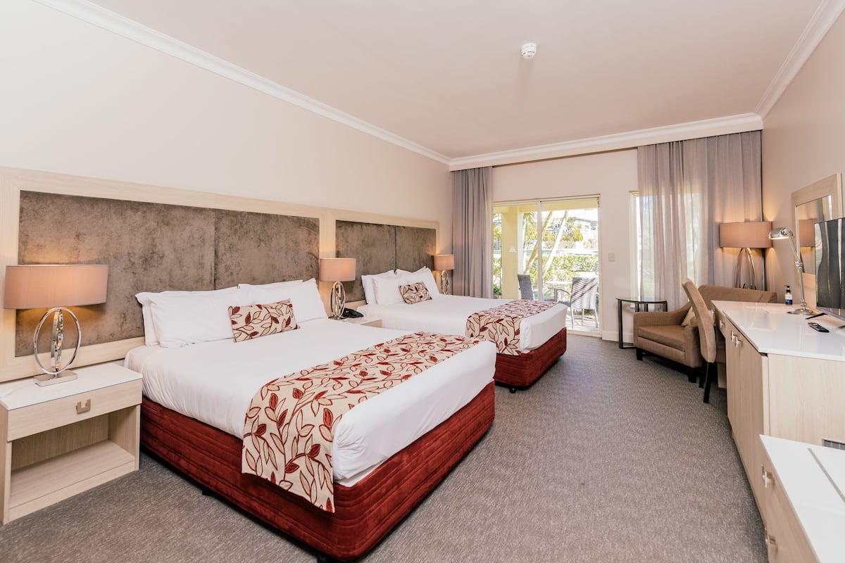 A hotel room with two beds, a desk, a chair, and a large window.
