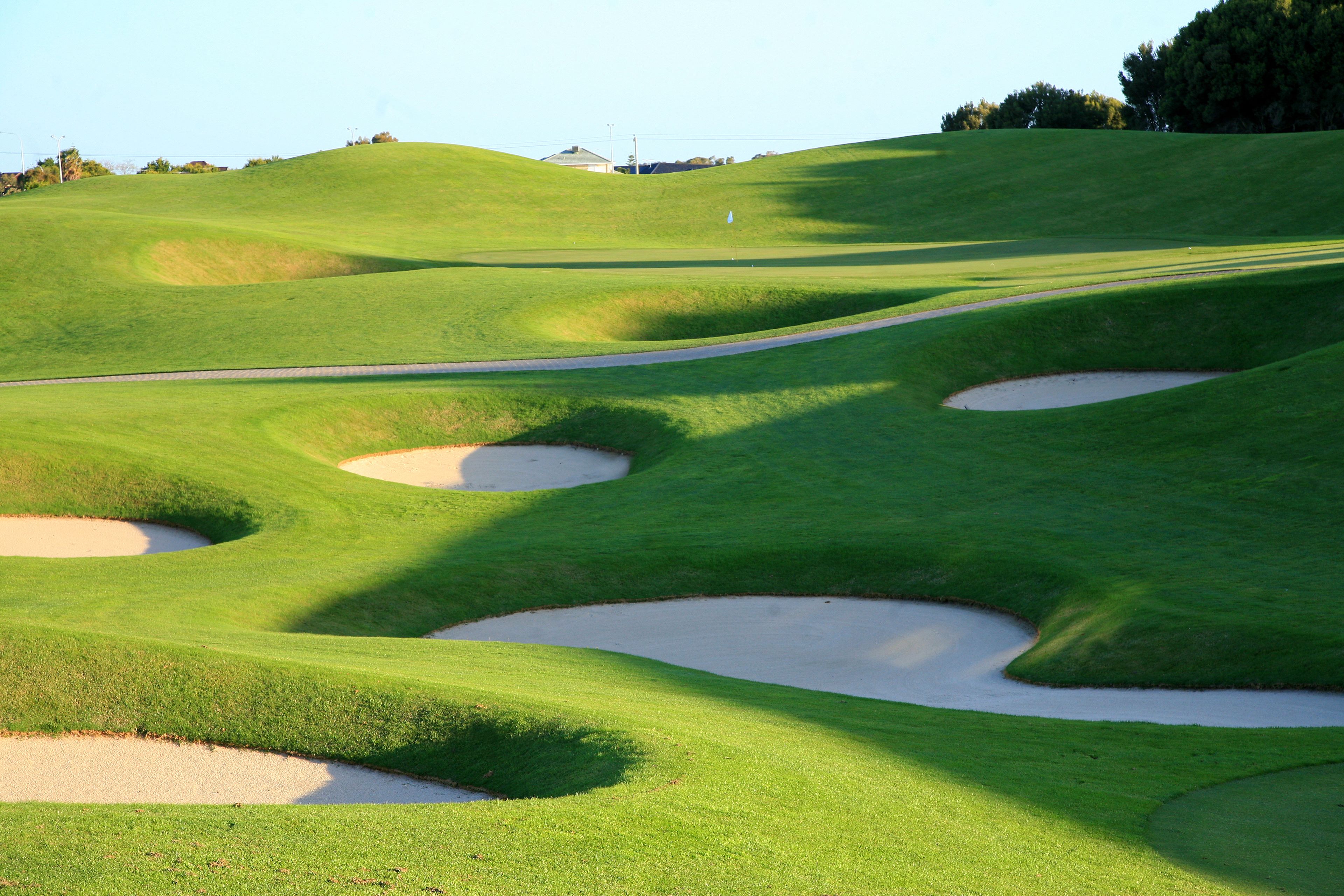 A golf course with sand bunkers and a clear sky.