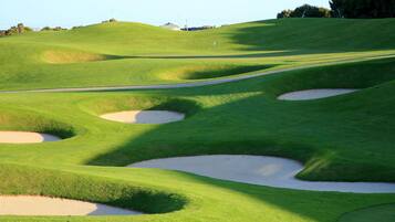A golf course with sand bunkers and a clear sky.
