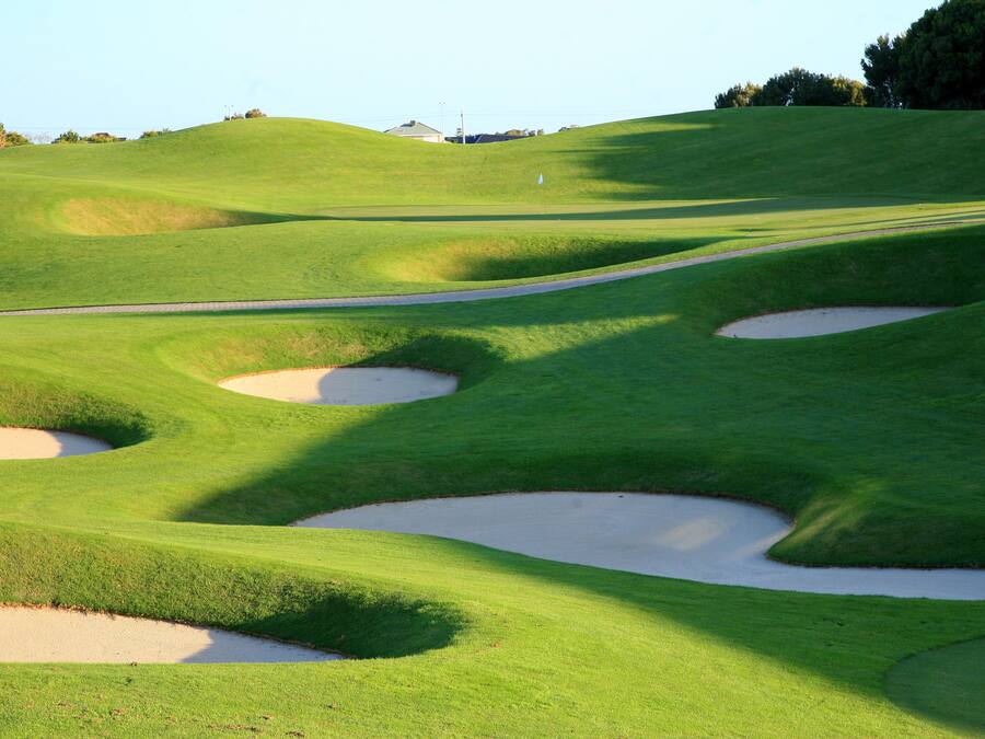 A golf course with sand bunkers and a clear sky.