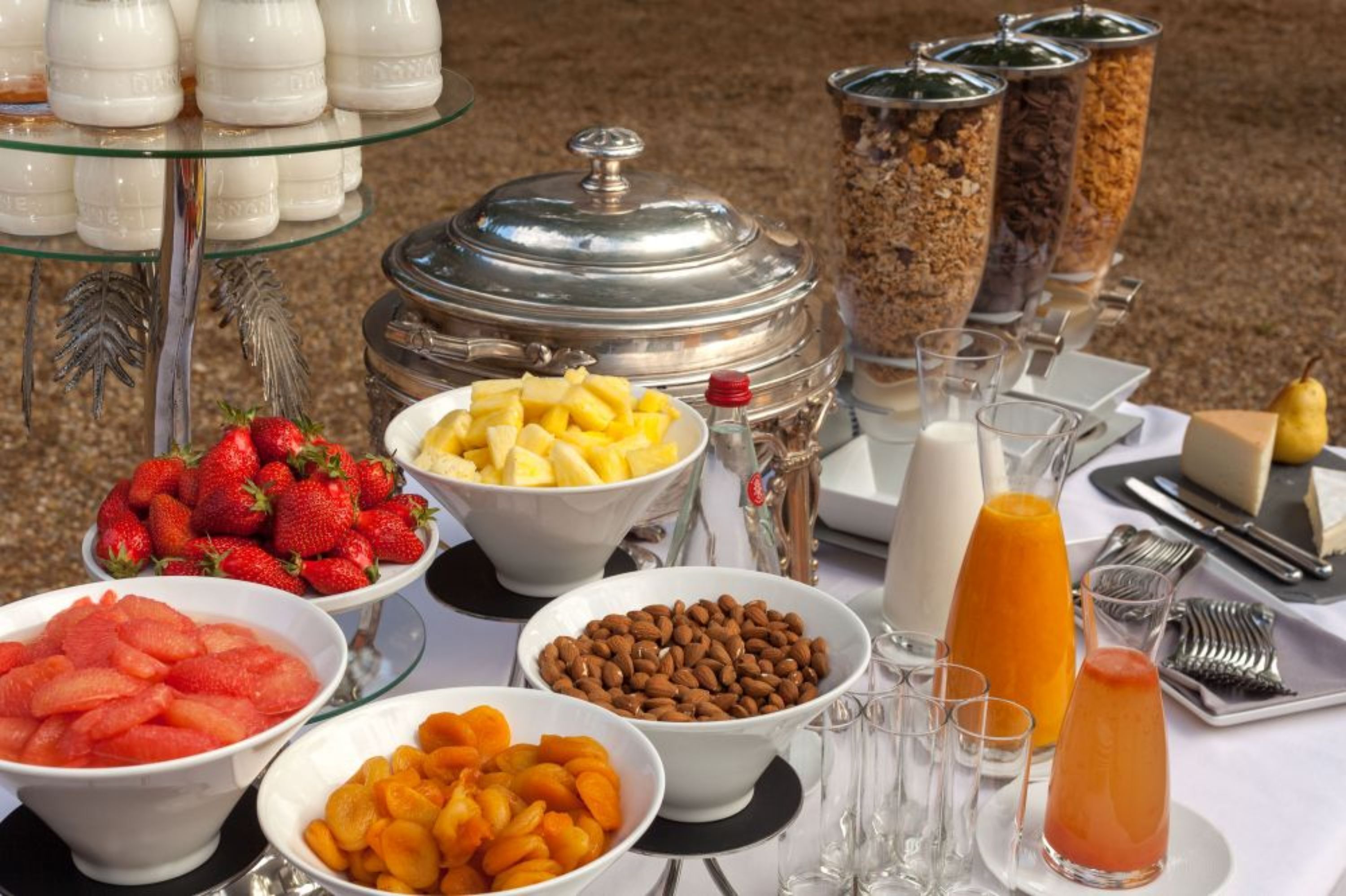 Una mesa de buffet con diversos alimentos, incluyendo frutas, frutos secos y un dispensador de jugo.