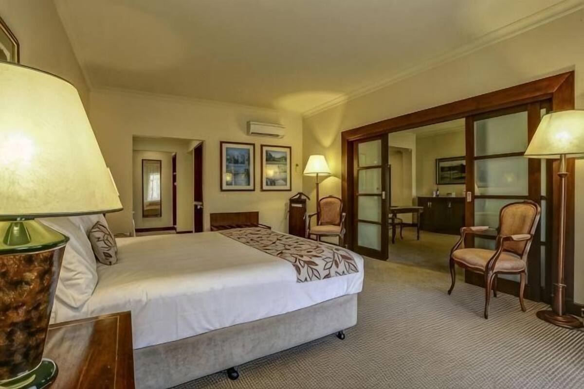 A hotel room with a bed, two chairs, a desk, and a door leading to a balcony.