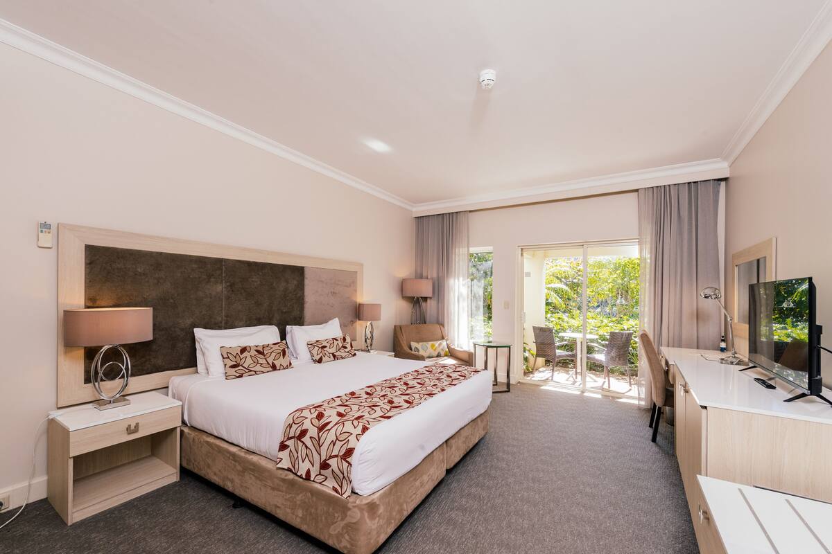 A hotel room with a large bed, bedside lamps, a desk with a TV, and a view of the outdoors.