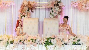 Two cushioned chairs sit beneath a floral arch, surrounded by elegant drapery.