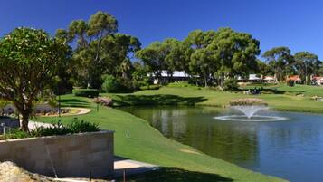 Un campo de golf con un estanque, árboles y una fuente.