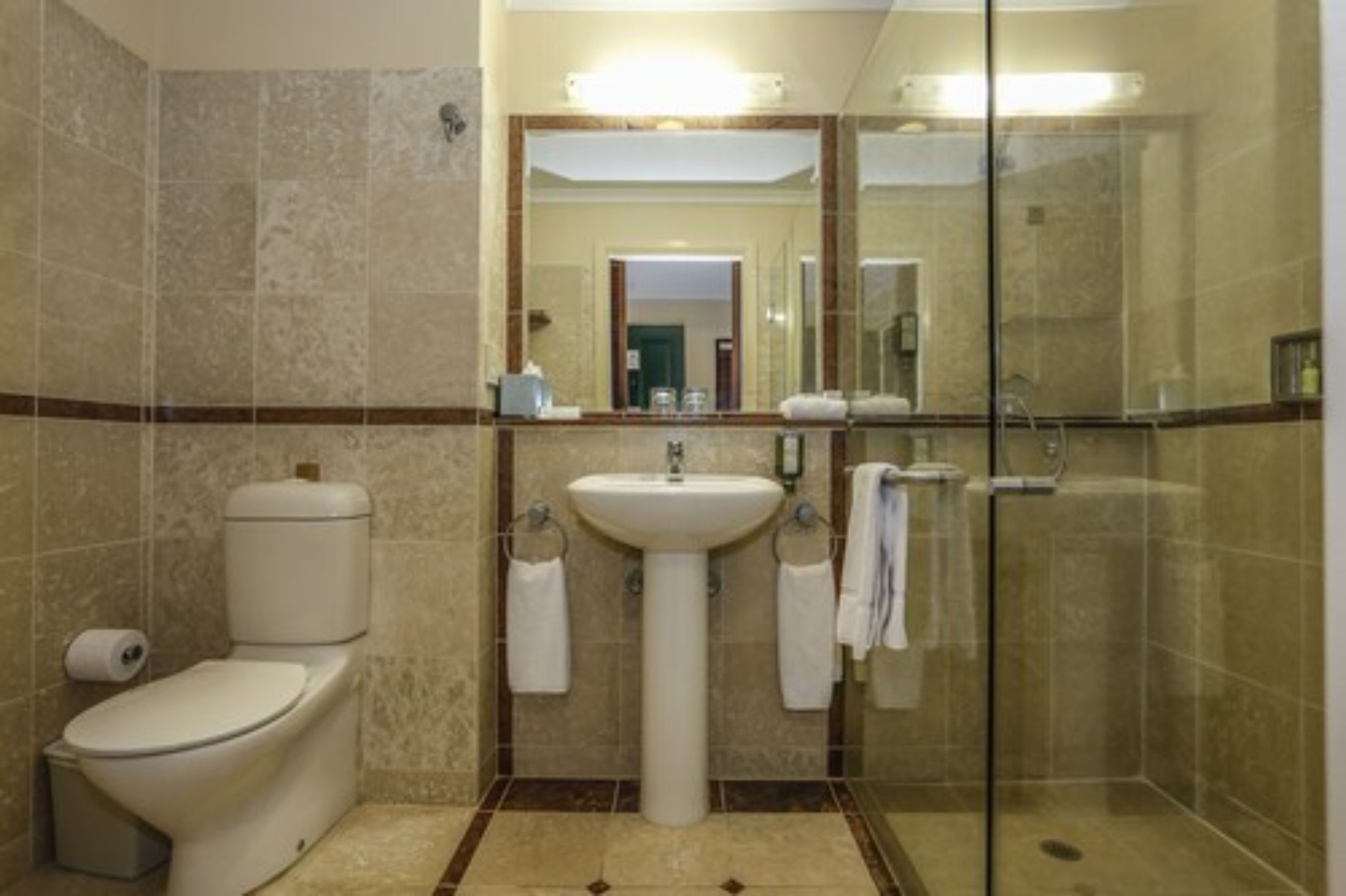 A bathroom with a toilet, sink, and glass shower enclosure.