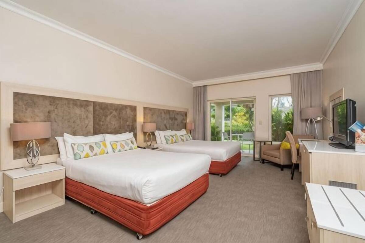 A hotel room with two beds, a desk, a chair, a TV, and a window with a view.
