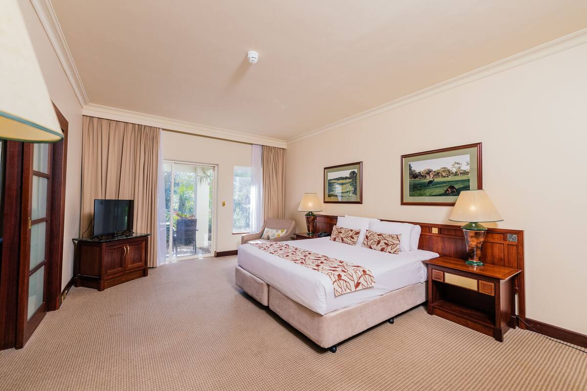 A hotel room with a large bed, two bedside tables, a television, and a view of the outdoors through a sliding door.
