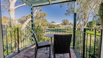 Un espacio de estar al aire libre cubierto con una mesa y sillas, con vistas a un parque con árboles y un edificio lejano.