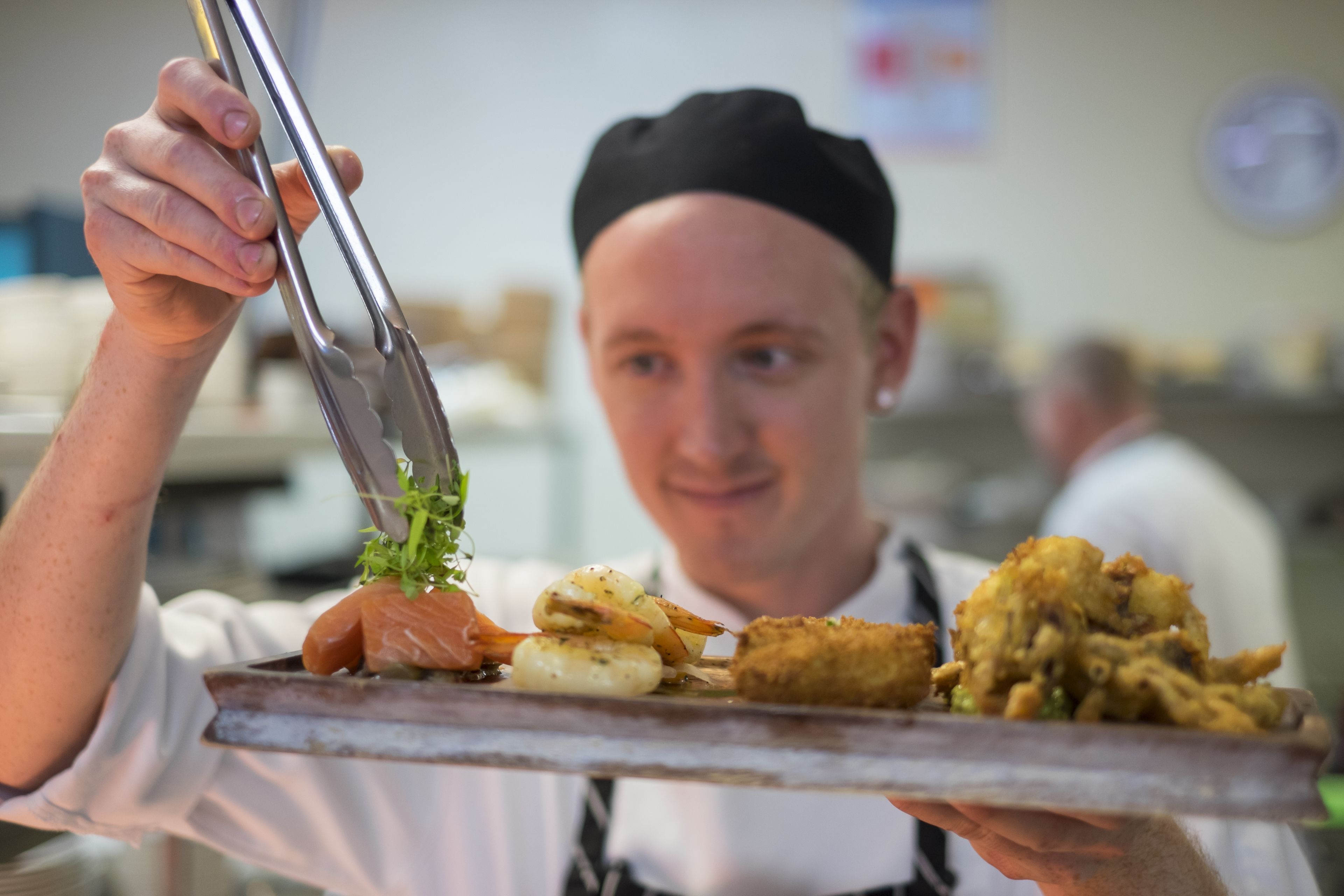 A person holding a tray with various food items, including a piece of salmon and some fried items.