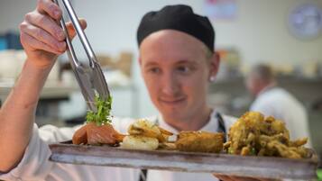 A person holding a tray with various food items, including a piece of salmon and some fried items.