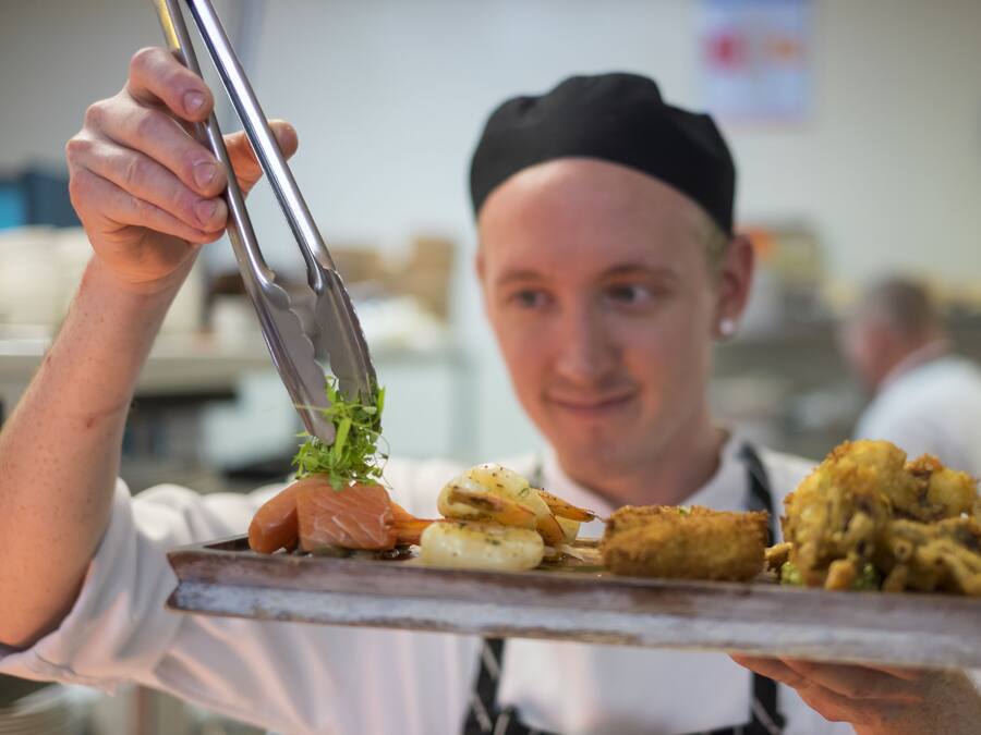A person holding a tray with various food items, including a piece of salmon and some fried items.