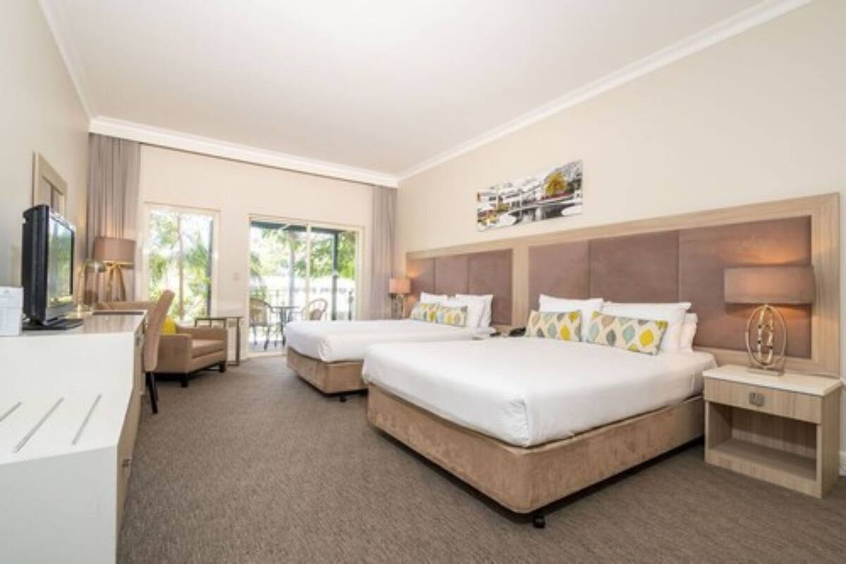 A hotel room with two beds, a desk, a chair, and a TV.