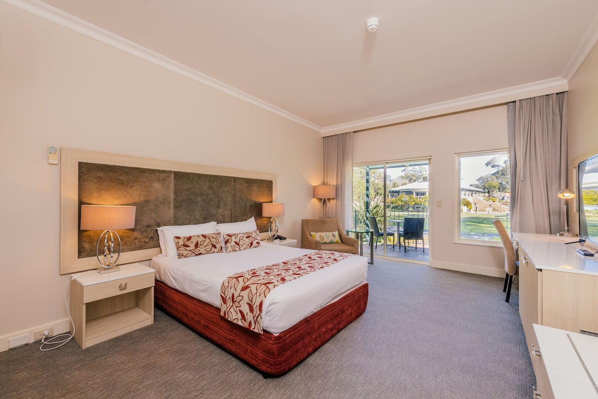 A hotel room with a large bed, bedside tables, a desk, and a view of the outdoors.
