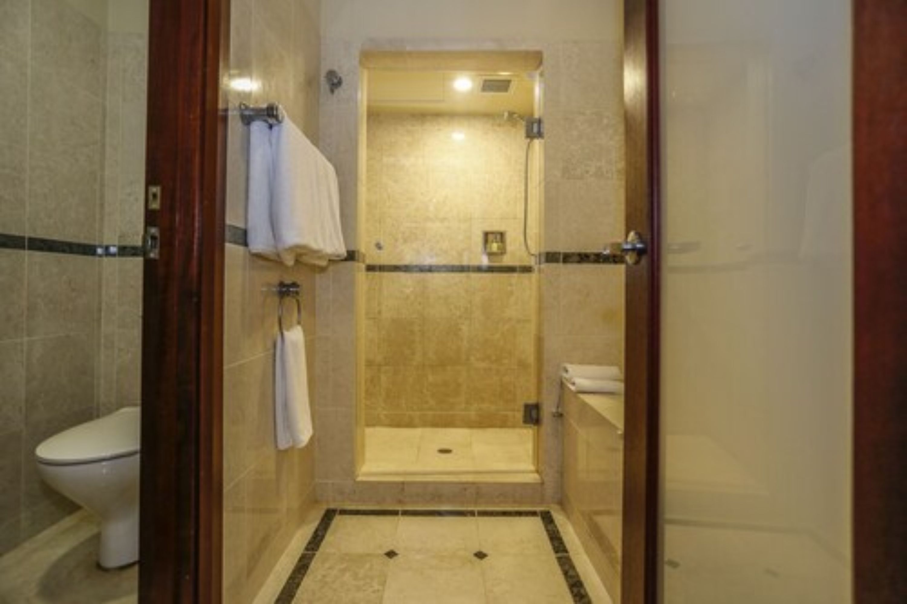 A glass-enclosed shower stall with a tiled floor, a white toilet, and a towel hanging on the wall.