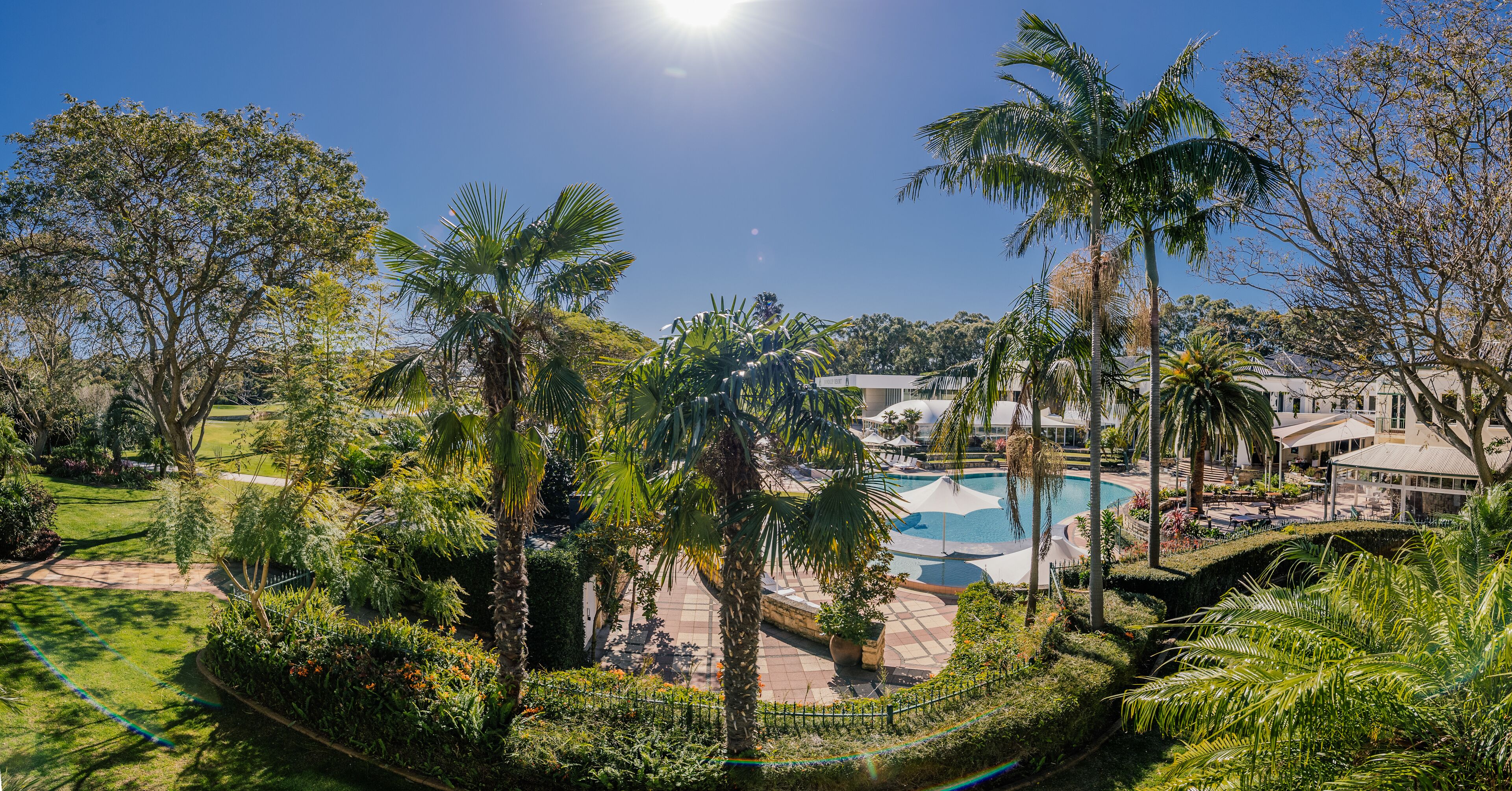 A resort with a swimming pool, palm trees, and a well-maintained garden.