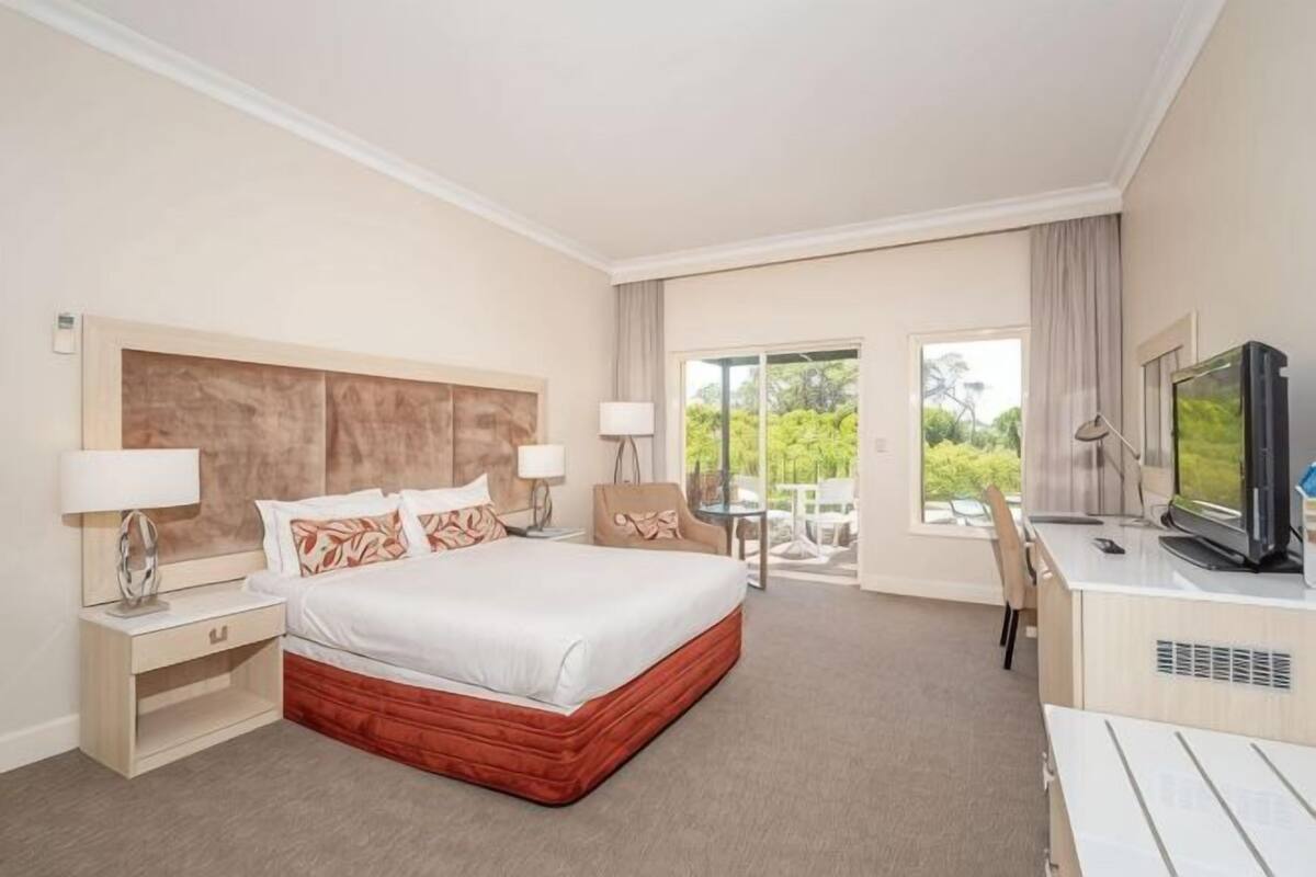 A hotel room with a large bed, bedside tables with lamps, a TV, and a balcony with a view.