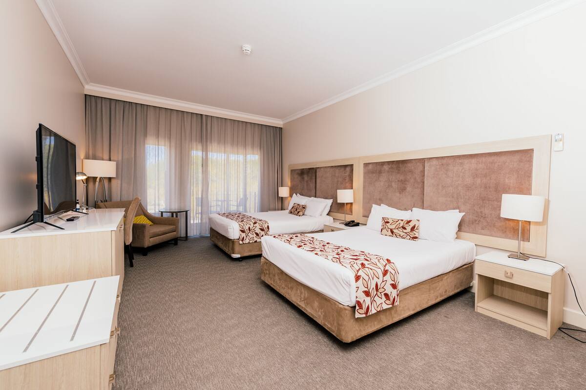 A hotel room with two beds, a desk, a TV, and a sofa.