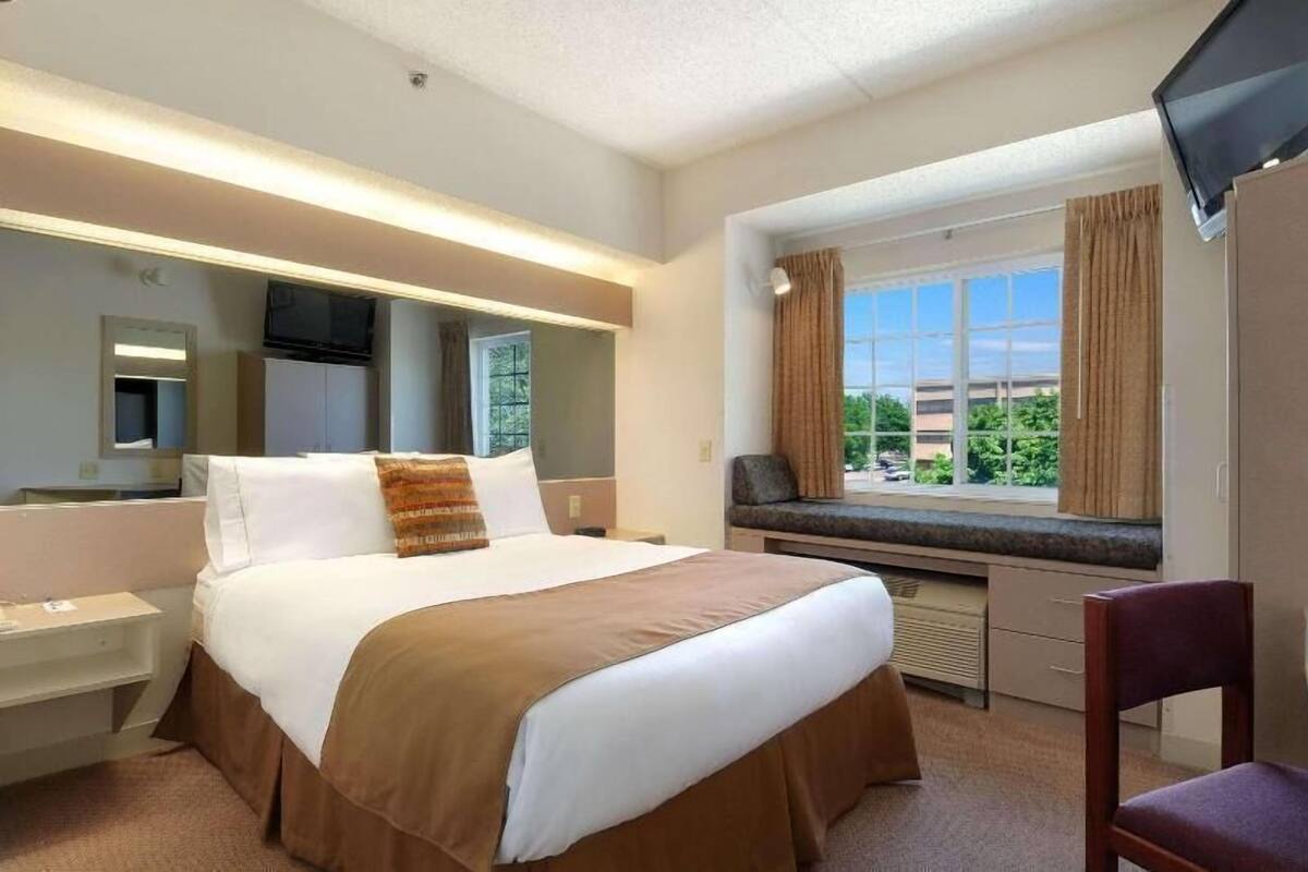 Une chambre d’hôtel avec un lit, une télévision, une fenêtre avec des rideaux, un bureau et une chaise.