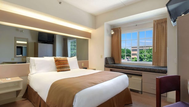 A hotel room with a large bed, a desk, a chair, a TV, and a window with curtains.