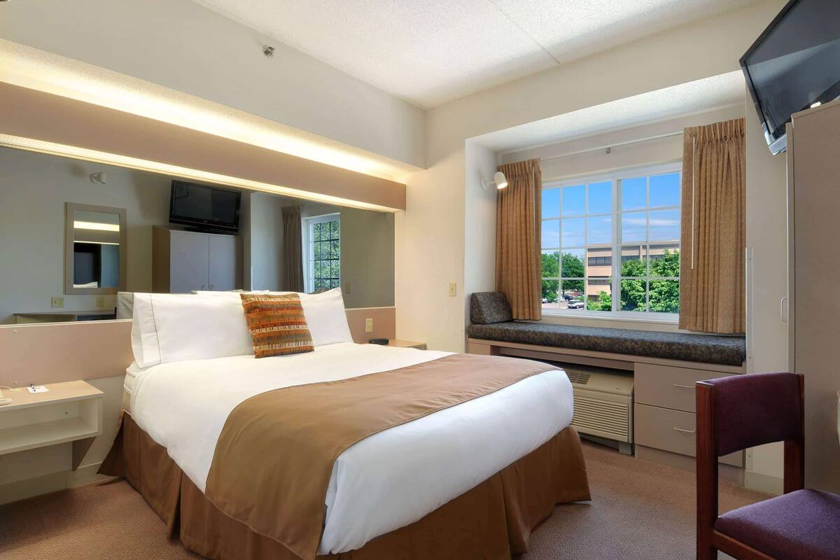 Une chambre d’hôtel avec un grand lit, un bureau, une chaise, une télévision et une fenêtre avec des rideaux.