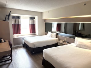 Habitación de hotel con dos camas, un escritorio, una silla, un armario y una ventana con cortinas.