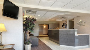 A reception area with a reception desk, a television mounted on the wall, a potted plant, and a lamp.