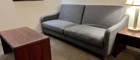 A grey sofa, a wooden side table, and a lamp on a carpeted floor.