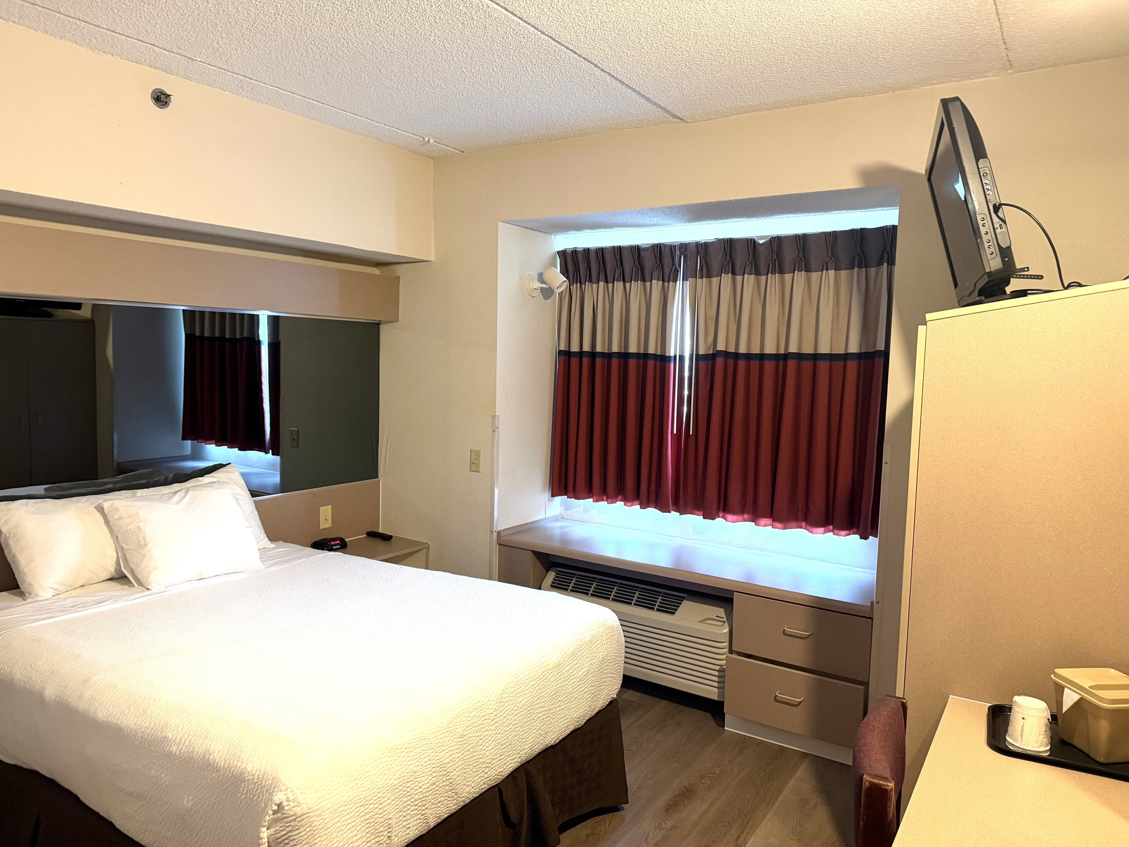 A hotel room with a bed, a desk with a computer, a television, and a window with curtains.