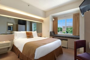 Een hotelkamer met een groot bed, een bureau, een stoel, een televisie en een raam met gordijnen.