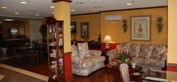 A lobby with two patterned sofas, a wooden bookcase, and a dining area with chairs and a table.