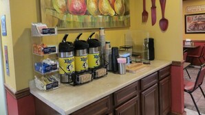 A breakfast bar with coffee dispensers, a painting of pears, and a sign that says "Eat".