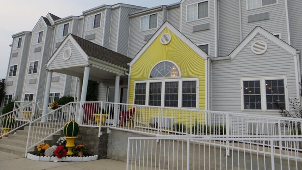 A multi-story hotel with a distinctive yellow and gray facade, a covered entrance, and a white railing in front.