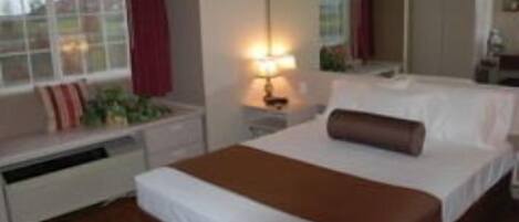 Habitación de hotel con una cama grande, una mesita de noche con lámpara, una ventana con cortinas y vistas al exterior.