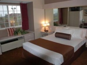 A hotel room with a large bed, a bedside table with a lamp, a window with curtains, and a view of the outdoors.