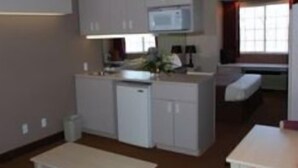 A compact kitchen with a microwave, a small refrigerator, and a sink. There is a dining table and a bench in the adjacent living area.