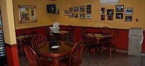 A restaurant with round tables and chairs, framed pictures on the wall, and a trash can.