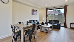 A modern living room with a dining table, two sofas, and a large window with curtains. - Comfort Hotel Dandenong (Dandenong)