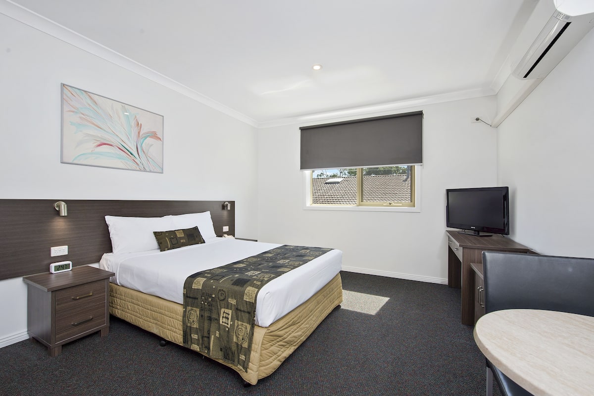 Een hotelkamer met een bed, nachtkastje, televisie en een raam met uitzicht.