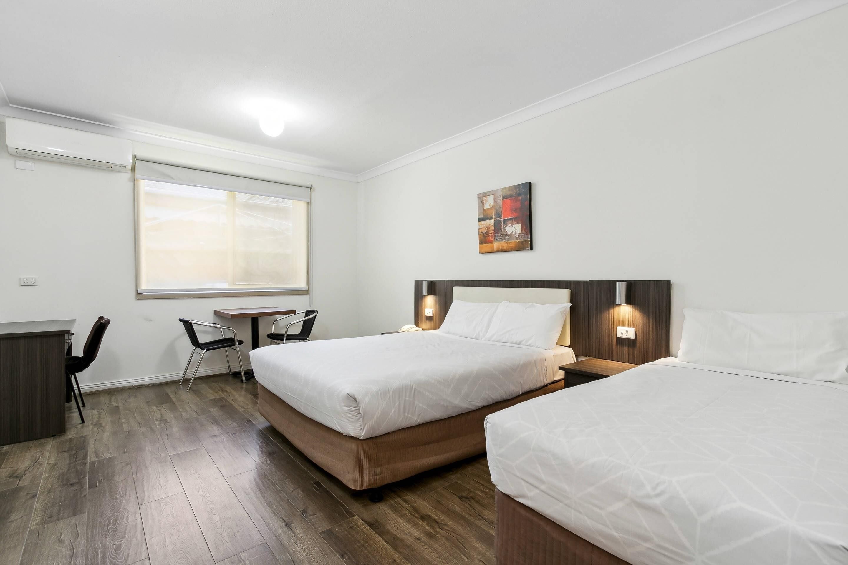 A hotel room with two beds, a desk, and a chair.