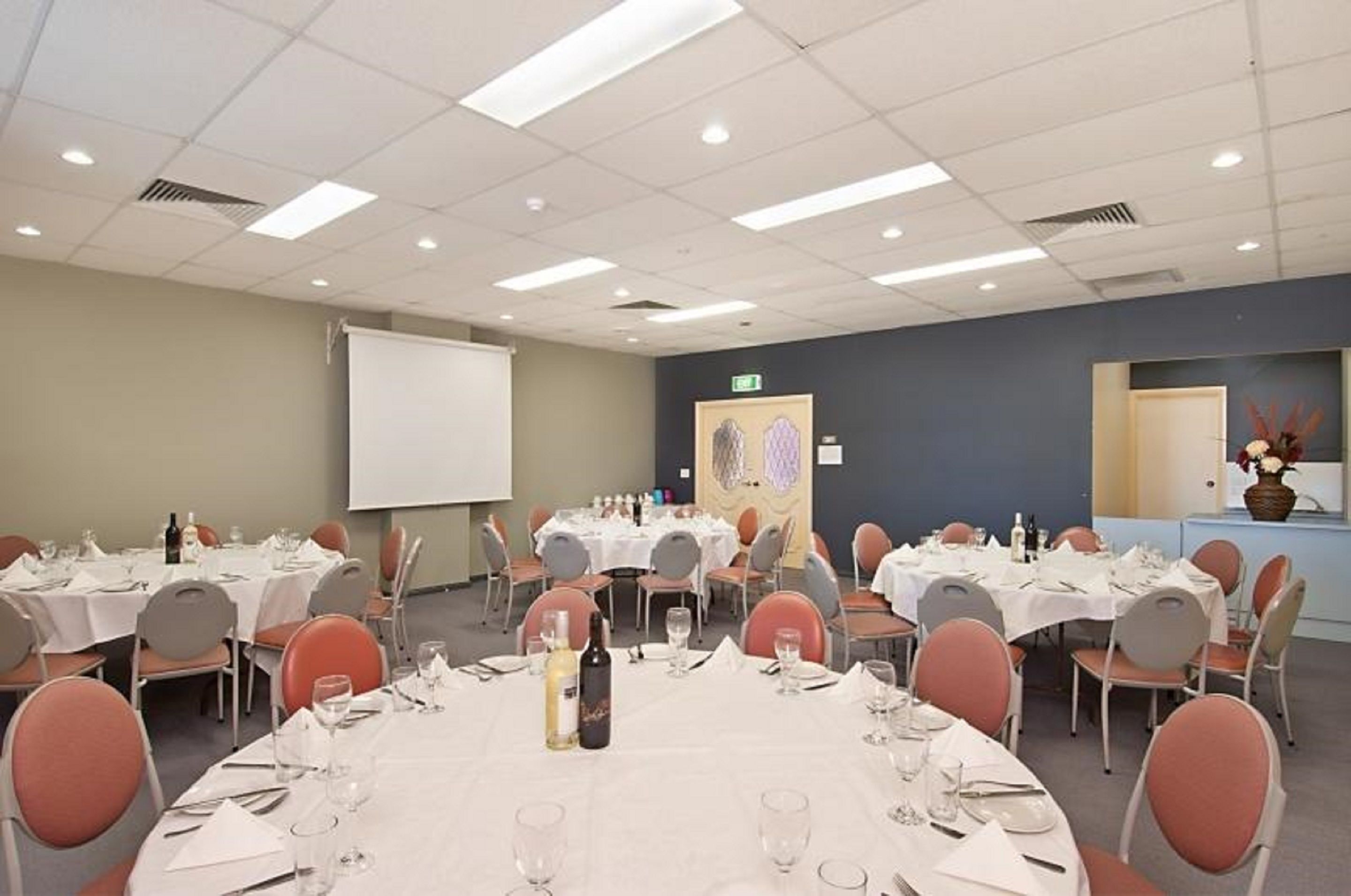 A conference room with multiple round tables set for dining, equipped with chairs and table settings.