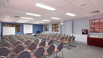 Un salón de conferencias con filas de sillas, una pizarra y una pantalla para proyector.