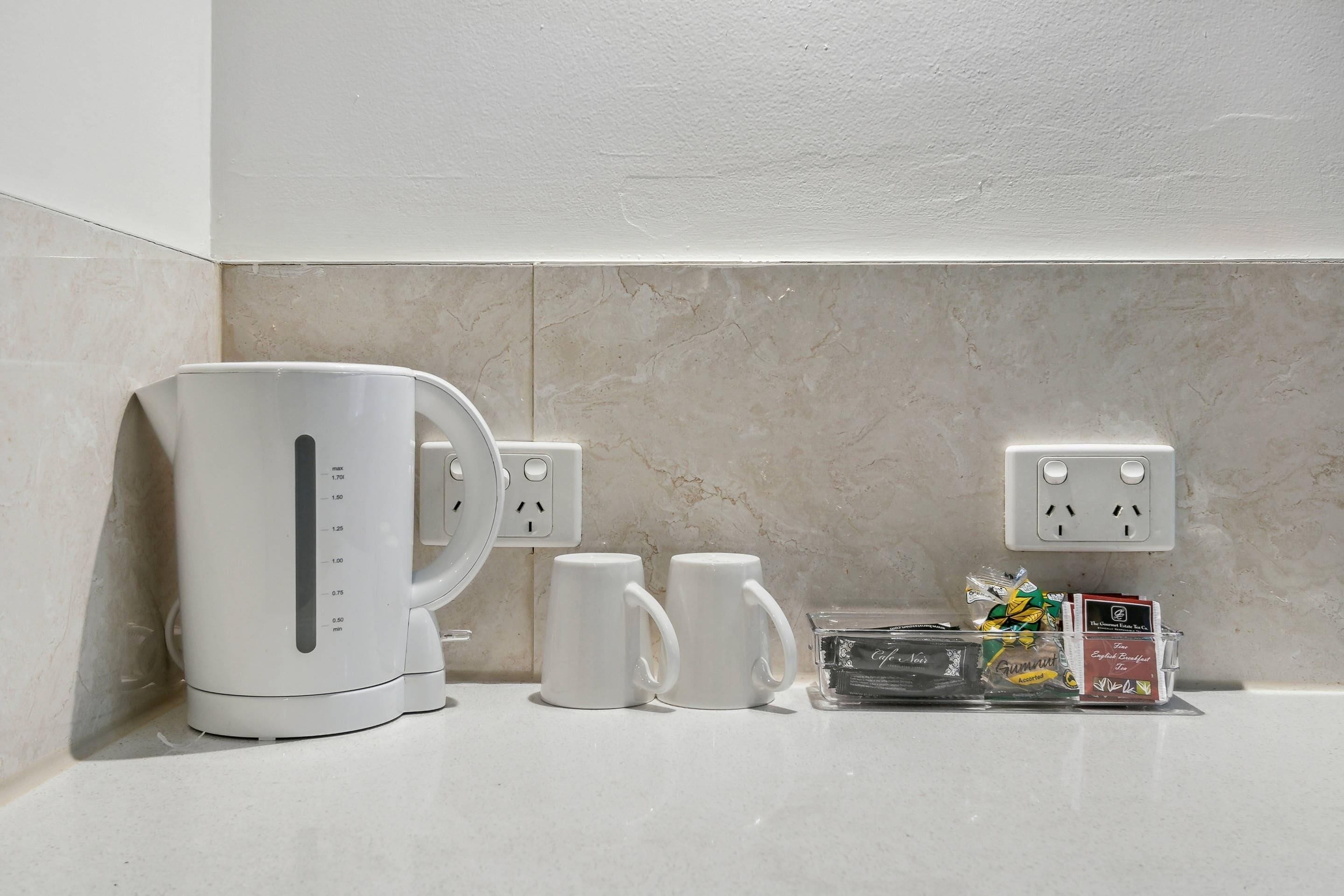 A kitchen counter with a coffee maker, two white mugs, and a box of assorted coffee pods.
