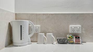 A kitchen counter with a coffee maker, two white mugs, and a box of assorted coffee pods.