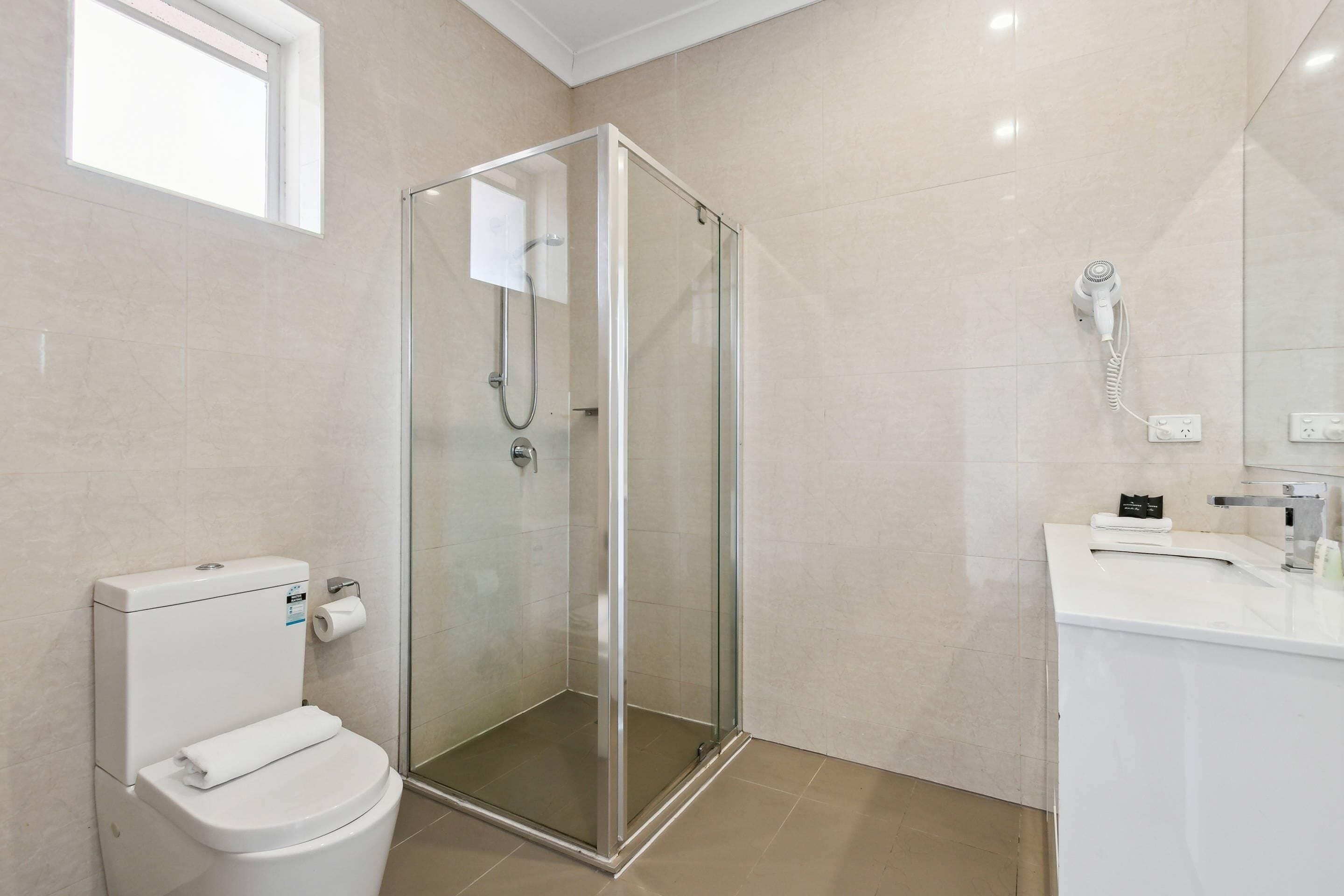A modern bathroom with a glass-enclosed shower, a white toilet, and a sink with a mirror.