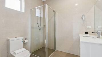 A modern bathroom with a glass-enclosed shower, a white toilet, and a sink with a mirror.