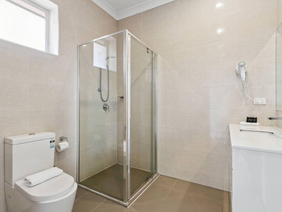 A modern bathroom with a glass-enclosed shower, a white toilet, and a sink with a mirror.