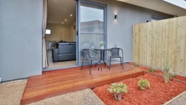 A modern outdoor patio with a wooden deck, a small table and chairs, and a garden area with red mulch and plants. - Comfort Hotel Dandenong (Dandenong)